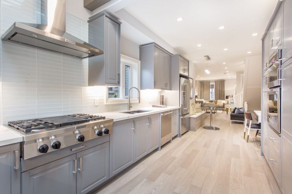 Fully finished renovation to galley kitchen with white tile backsplash and grey cabinets.