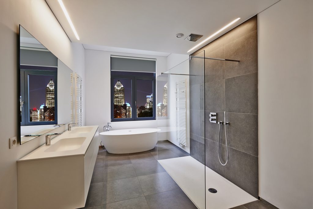 Renovated Bathtub in corian, Faucet and curbless shower in tiled bathroom with windows towards night city lights
